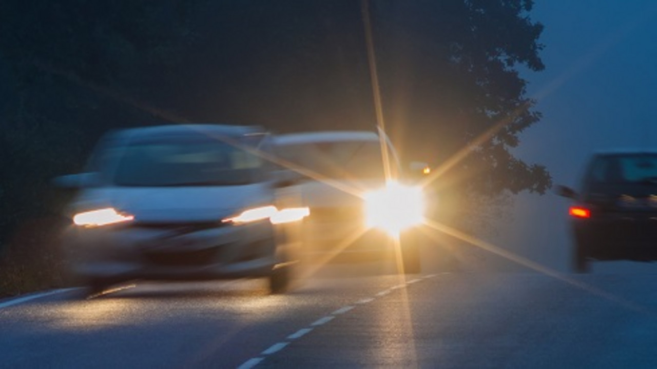 Drei Autos fahren mit eingeschaltetem Licht in der Dämmerung über eine Landstraße