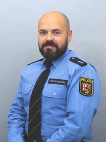 Freundliches Portrait eines männlichen Polizisten in Uniform mit Glatze und dunklem Bart Bart