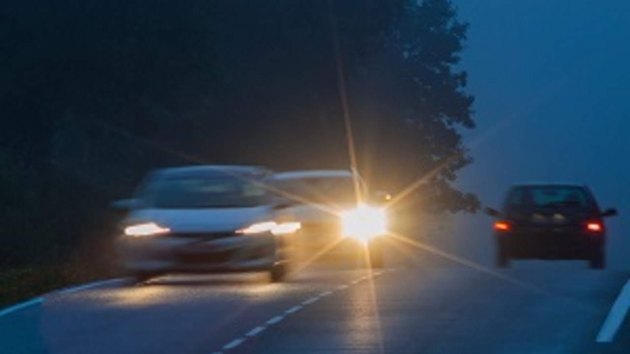 Drei Autos fahren mit eingeschaltetem Licht in der Dämmerung über eine Landstraße