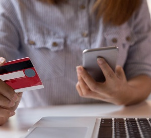 Frau vor Laptop mit Smartphone und Kreditkarte in der Hand
