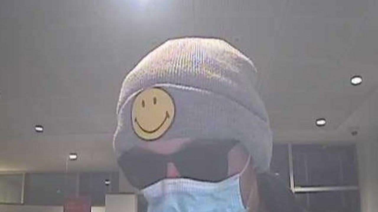 Der unbekannte Täter. Er trägt einen Mund-Nasen-Schutz, eine Sonnenbrille und eine Mütze mit einem gelben Smiley Patch.