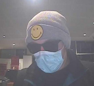 Der unbekannte Täter. Er trägt einen Mund-Nasen-Schutz, eine Sonnenbrille und eine Mütze mit einem gelben Smiley Patch.