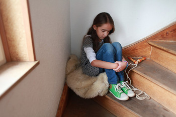 Traumatisiertes Kind sitzt auf einer Treppe mit verschränkten Armen.