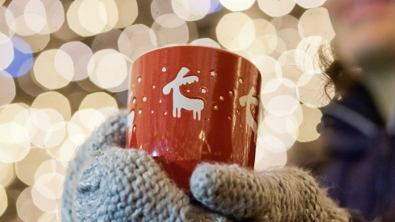 Frau mit einer Tasse in der Hand. Im Hintergrund Weihnachtsbeleuchtung.