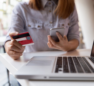 Eine Frau schaut auf ihr Smartphone und hält in der anderen Hand eine Kreditkarte