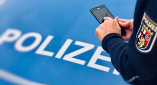 Polizist steht vor Streifenwangen mit Handy in der Hand