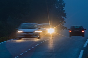 Drei Autos fahren mit eingeschaltetem Licht in der Dämmerung über eine Landstraße