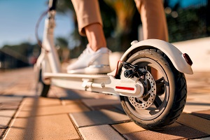 Eine Frau auf einem E-Scooter. Man sieht nur den Fuß der Frau auf dem E-Scooter.