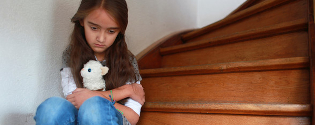 Trauriges Kind mit Kuscheltier sitzt auf einer Treppe