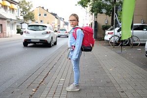 Kind mit Schulranzen steht auf dem Bürgersteig an einer Straße