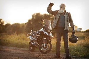 Ein älterer Mann steht vor seinem Motorrad mit einem Motorradhelm in der Hand