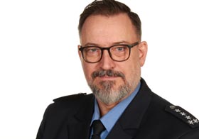 Portraitaufnahme eines Polizisten in Uniform. Er trägt eine Brille, hat ein grau melierten Bart und kurze, braune Haare
